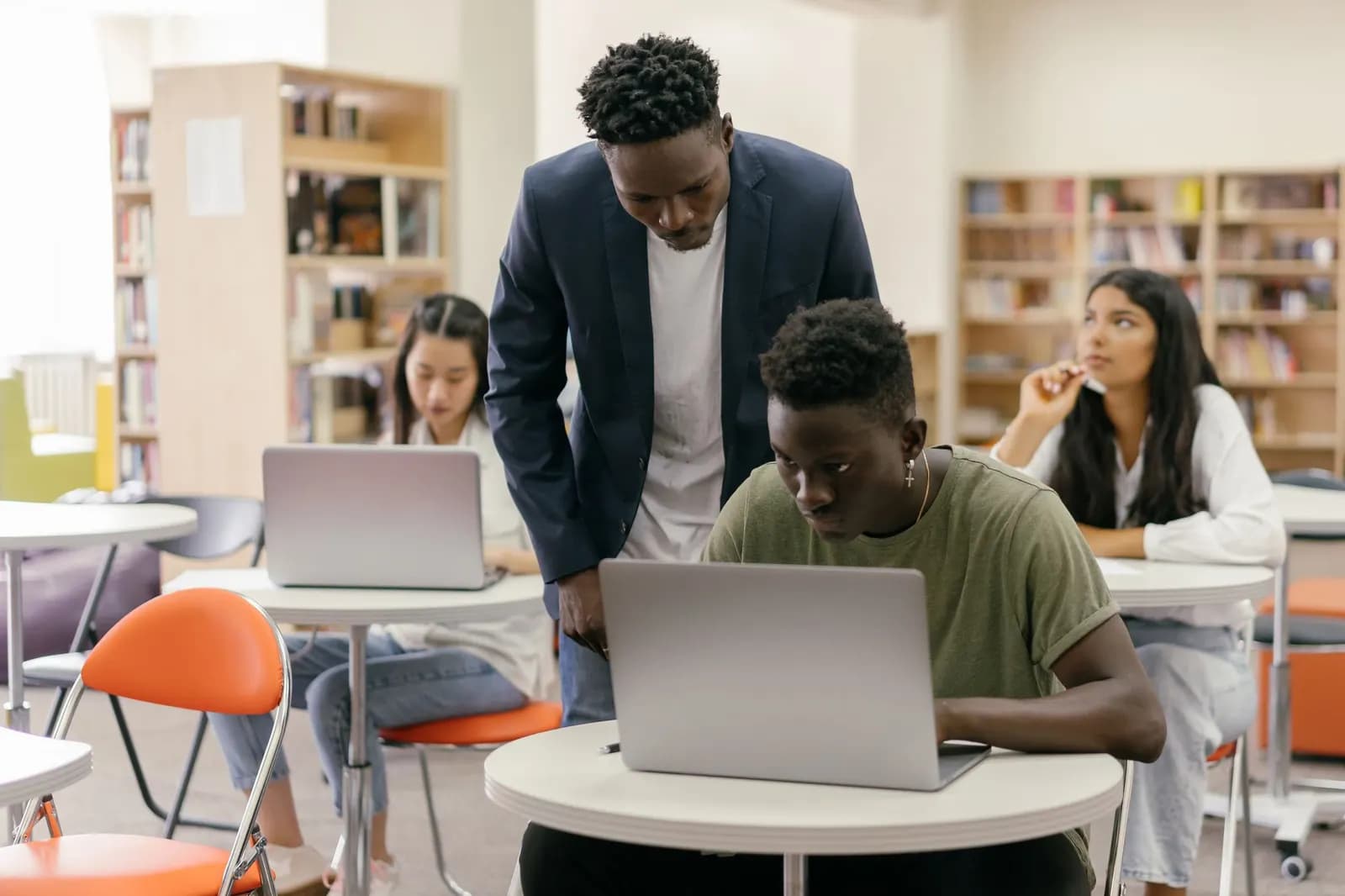 A lecturer in a blazer looking over students' work at laptops in a bright classroom