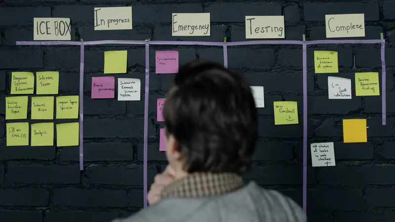 A person reviewing a task board of sticky notes in columns from in progress to complete.
