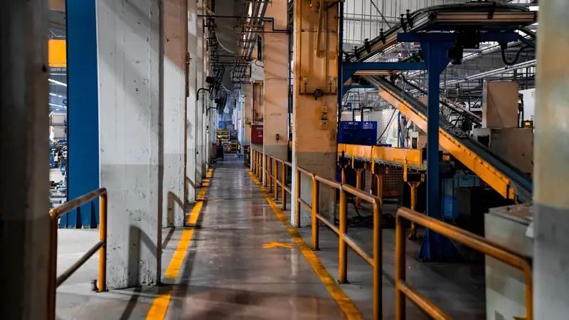 A walkway with yellow floor markings and railings through a factory floor.